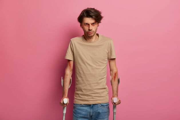 人严重扭伤的男人 在意外情况下尝试行走和恢复 仔细听取医生的建议 穿着休闲服 在粉色墙壁上摆姿势医疗保健和医疗支持概念腿康复墙