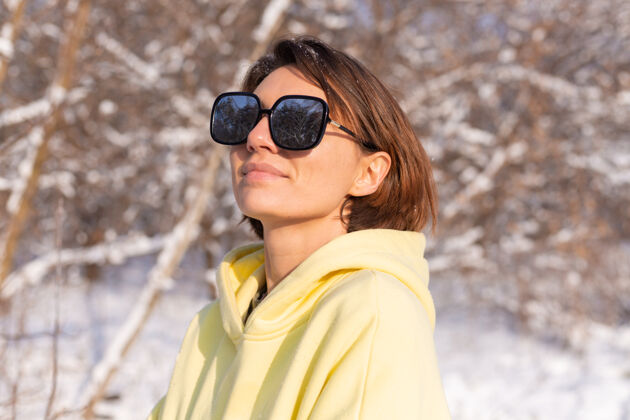 冬天阳光明媚的日子里 雪景冬林中一位年轻美女的画像 身着黄色大套头衫 戴着墨镜 享受着阳光和雪太阳娱乐漂亮