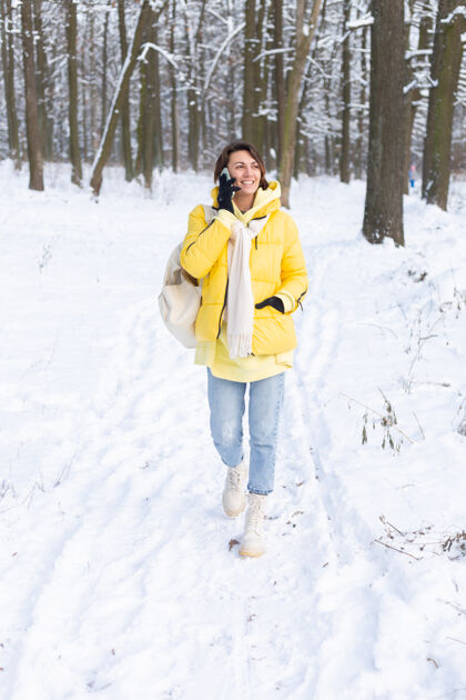 美丽心情愉快的快乐女人漫步在雪域的冬日森林里 愉快地聊着电话 享受着公园里的户外时光季节女士微笑