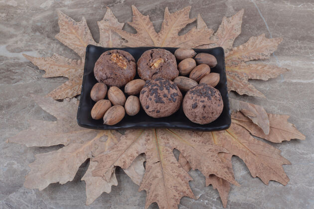 美味盘子里放着一捆饼干和山核桃 大理石上放着一捆梧桐树叶小吃拼盘坚果