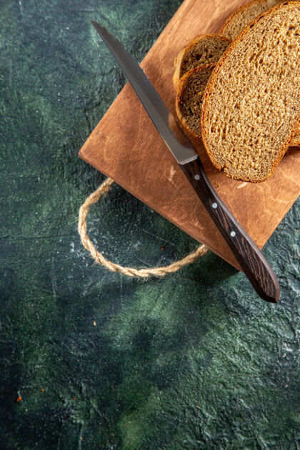 特写黑色面包刀的俯视图在黑暗的表面上的棕色木制切割板上设备食物关闭