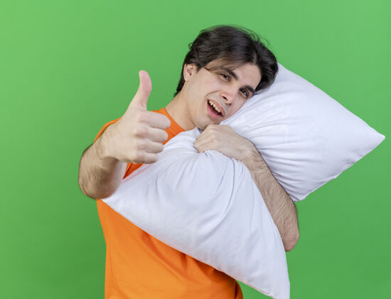 疾病快乐的年轻病人抱着枕头 在绿色的背景上孤立地竖起大拇指年轻拥抱枕头