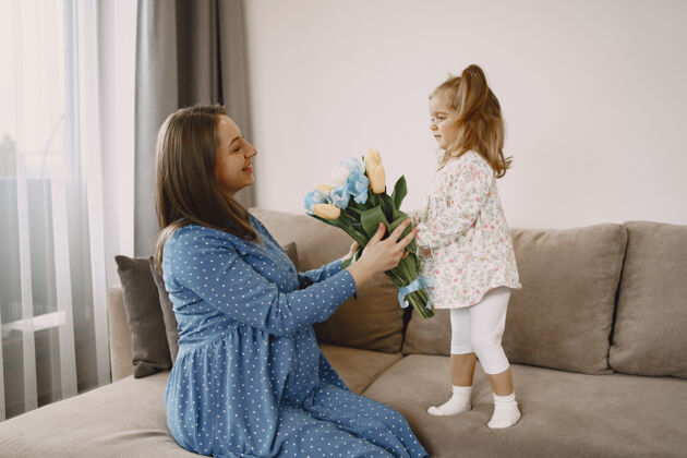 问候带着鲜花的女儿躺在沙发上的怀孕妈妈穿着鲜艳衣服的妈妈和女儿怀孕快乐礼物