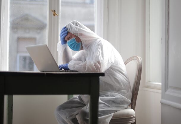 年轻人男性在一台有医疗服和面罩保护的电脑上工作工人危险商人