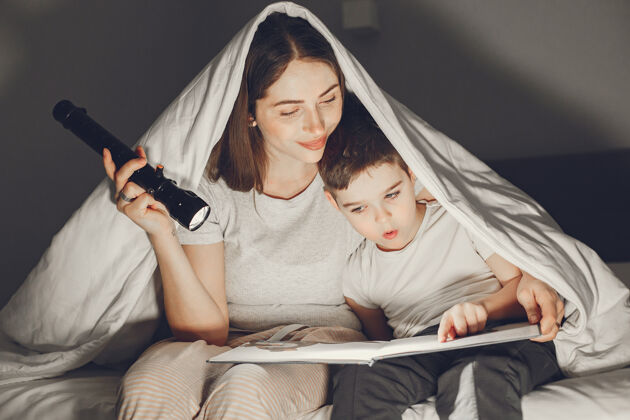 阅读母子俩在毯子下躺在床上看书灯休闲婴儿