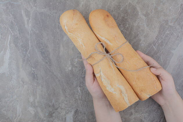 糕点手拿着半块法式面包放在大理石表面地壳美味食品