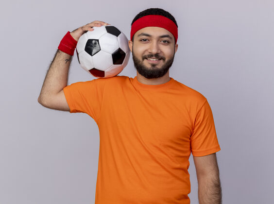 球微笑的年轻人戴着头带和腕带 肩上拿着球 背景是白色的运动年轻肩膀