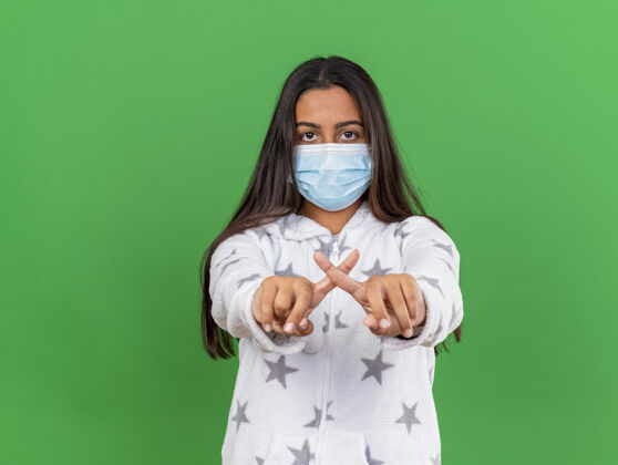 年轻年轻的生病女孩戴着医用口罩看着镜头 在绿色背景上显示出不孤立的姿态女孩手势面具