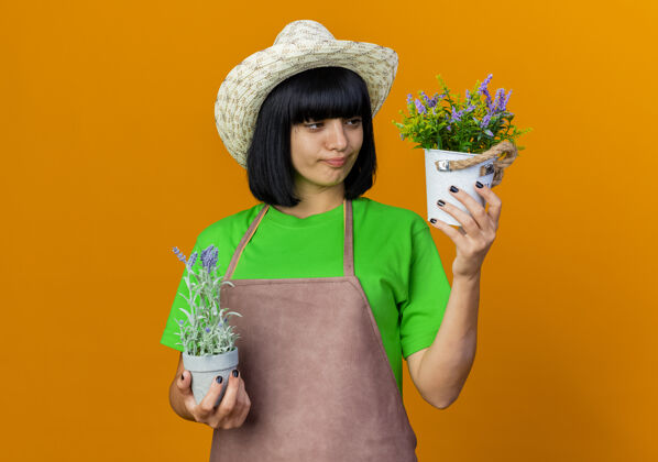 园艺体贴的年轻女园丁穿着制服 戴着园艺帽 拿着花盆看空间年轻穿着