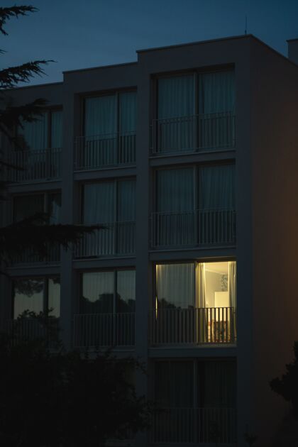 当代一个现代白色建筑的垂直镜头 灯光从一个大阳台窗户射出空的房子中心