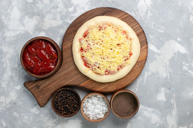 美食顶视图生比萨饼与奶酪和不同的调味品在白色食物烹饪新鲜