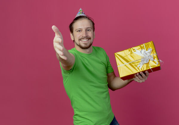 礼物戴着生日帽的微笑帅哥手拿礼盒 在粉色的墙上孤零零地伸出手来拿着手生日