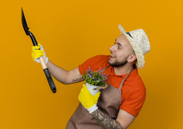 空间快乐的男园丁戴着园艺帽子和手套 手里拿着花盆里的花和铁锹看着旁边复制橘子手套