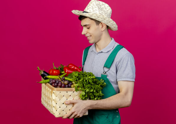 园艺高兴的年轻男园丁戴着园艺帽站在一旁 抱着菜篮看着穿年轻空间