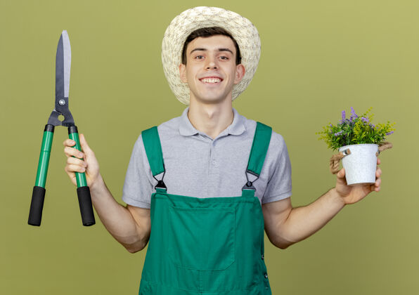 绿色微笑的年轻男园丁戴着园艺帽 手里拿着剪子和花盆里的花花园微笑男性