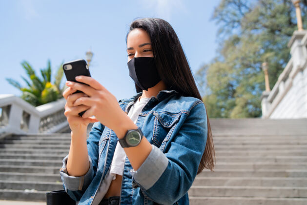 手机一张年轻女子戴着防护面具 站在街上用手机的照片一个智能年轻