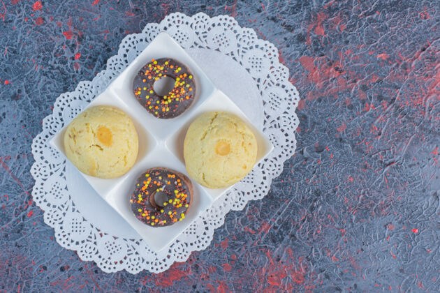 美味小吃大小的甜甜圈和饼干放在抽象桌上的小垫子上美味Doily曲奇饼