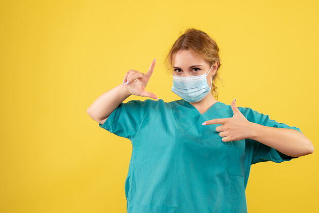大流行黄墙上穿着医疗服 戴着无菌口罩的女医生的正面图医疗脸人