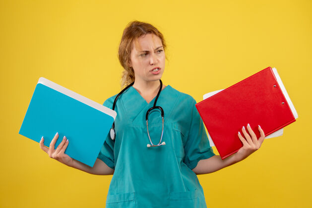 分析黄色墙壁上穿着医疗服的女医生拿着纸和分析的正视图健康病毒护士