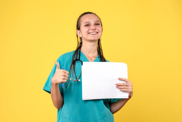 正面身穿医疗服的女医生在黄色的墙上拿着文件听诊器情绪医院