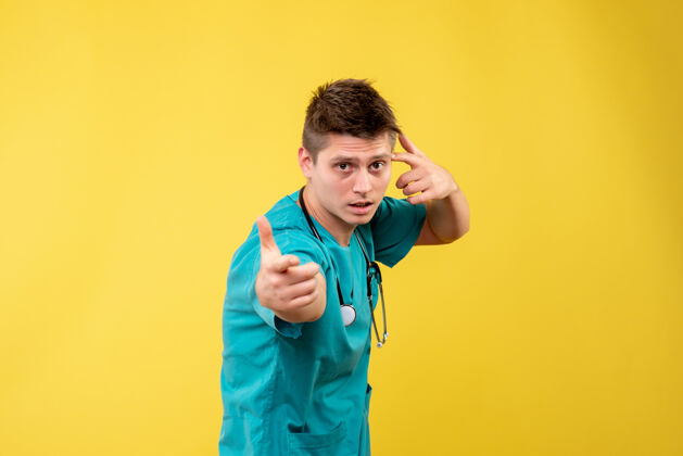 情绪黄色墙壁上穿着医疗服的男医生的正视图正面快乐套装