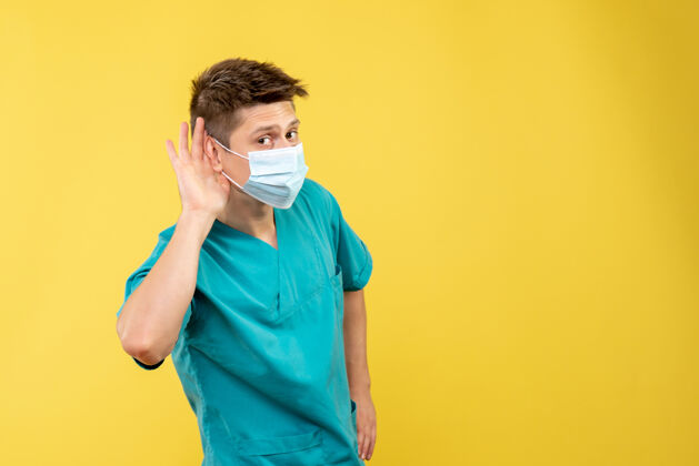 疾病身穿医疗服 戴着无菌口罩的男医生正对着黄色的墙壁聆听健康面具套装