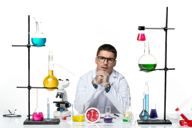 坐着正面图身着白色医疗服的男性化学家坐在白色背景病毒疾病科学实验室的不同解决方案上医学实验室病毒
