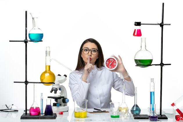 烧杯前视图穿着白色医疗服的女化学家拿着红色的时钟在白色背景上科学病毒实验室冠状病毒-大流行医学持有化学