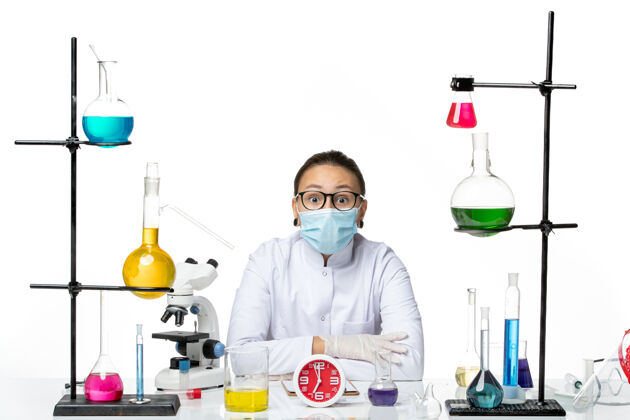 病毒前视图穿着医疗服的女化学家戴着面罩坐在白色背景上 溅起实验室病毒化学冠状病毒西装解决方案化学