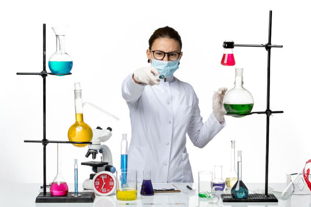 持有前视图：身穿医疗服的女化学家 戴着面罩 在白色背景上注射病毒化学实验室的covidsplash科学前面医生