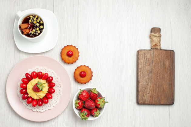 草莓俯瞰白色书桌上的奶油蛋糕和一杯茶水果小奶油蛋糕健康