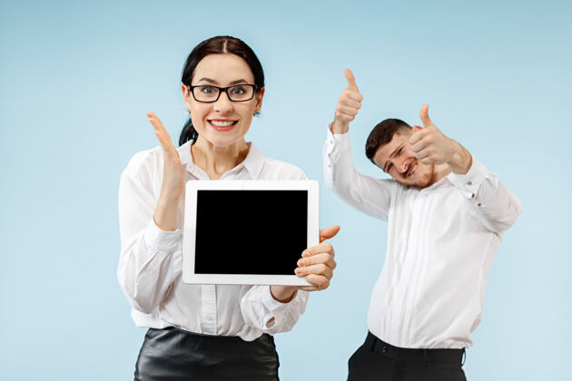 幽默在蓝色工作室背景上 惊讶的商务男女微笑着 展示着笔记本电脑或平板电脑的空屏幕成功表演微笑