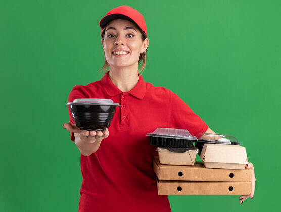 容器微笑着的年轻漂亮的送货女孩穿着制服拿着比萨饼盒上的纸食品包装和绿色的食品容器比萨饼人制服