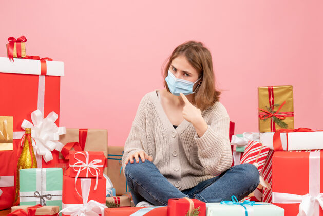 病毒正面图：坐在圣诞节周围的年轻女性戴着无菌面具出现坐着周围面具