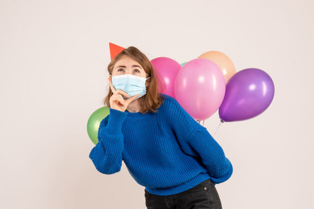 五颜六色正面图：戴着无菌口罩的年轻女性把五颜六色的气球藏在背后隐藏面具病毒