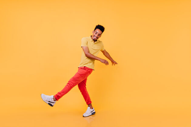 酷灵感来自穿着明亮休闲装的黑人 滑稽的舞蹈穿着黄色t恤和红色裤子的非洲男模在嬉戏舞蹈休闲卷发