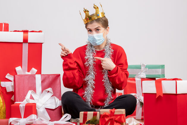坐着正面图年轻女性戴着面具和皇冠坐在那里 手里拿着圣诞礼物病毒圣诞节皇冠