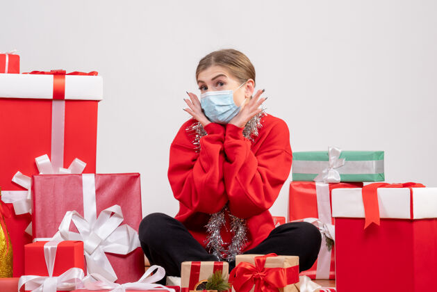 健康正面图：年轻女性戴着无菌面具坐着 手里拿着圣诞礼物圣诞节孩子面具