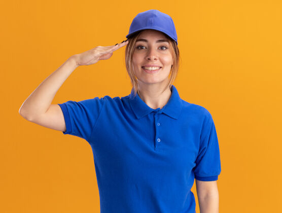 姿势微笑着的年轻漂亮的女送货员 穿着制服 在橘子上做着敬礼的手势漂亮制服敬礼