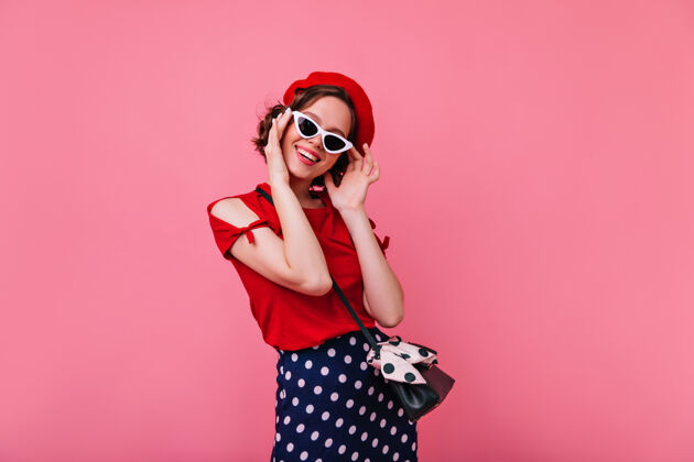 大笑俏皮的法国女人戴着太阳镜迷人的黑发女孩戴着红色贝雷帽在玫瑰色的墙上微笑人休闲欢呼
