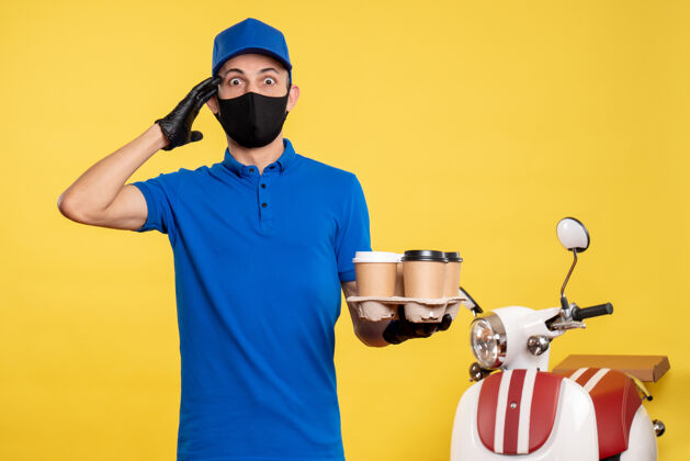 人正面图：戴着黑色口罩的男信使拿着咖啡 穿着黄色的送货工作服面具工作男性