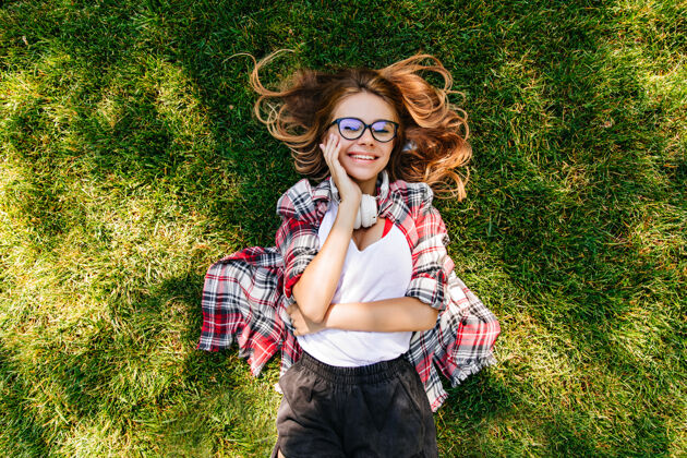 人满意的年轻女子在公园里表达幸福可爱女孩躺在绿草上的头像微笑女人自然