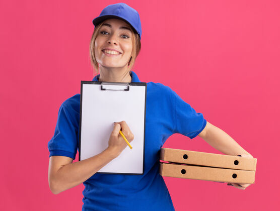 姿势微笑着的年轻漂亮的送货女孩 穿着制服 手里拿着剪贴板和粉红色的比萨饼盒披萨剪贴板送货