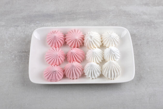 新鲜石头桌上摆着一盘白色和粉色的酥皮糖糕点自制脆