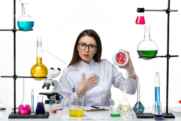 人前视图穿着白色医疗服的女化学家手持浅白色背景上的红色时钟科学病毒冠状病毒-大流行实验室烧杯前面持有