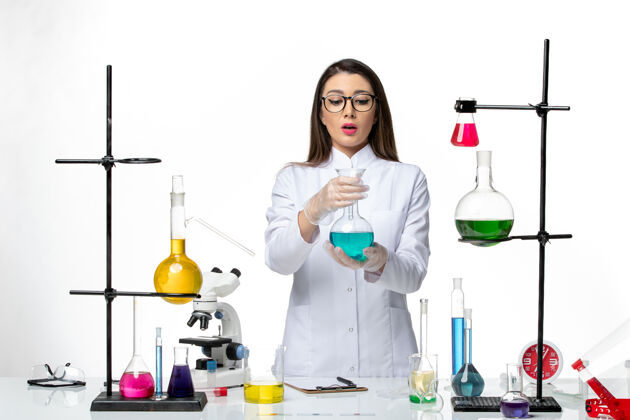 前面正面图：穿着无菌医疗服的女化学家拿着白色背景病毒冠状病毒溶液的烧瓶-大流行科学人病毒解决方案