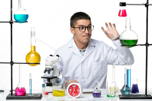 大流行正面图身穿白色医疗服的男性化学家坐在白色办公桌上 拿着解决方案病毒科学病毒大流行实验室实验室坐着办公桌