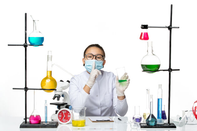 解决方案正面图白色办公桌上穿着医疗服的女化学家戴着口罩拿着溶液溅实验室病毒化学covid-设备病毒面罩