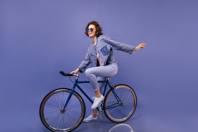 摩托车手穿着春装的神奇女人坐在自行车上戴着太阳镜的可爱女孩的室内写真紫色乐趣快乐