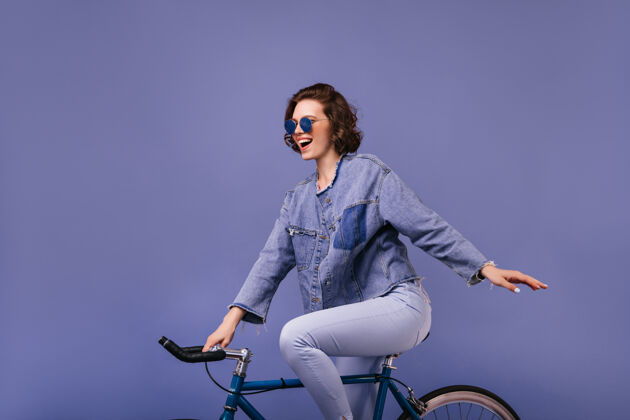 波浪发兴奋迷人的女人在自行车上摆姿势令人惊叹的女自行车手孤立的室内照片紫色女士配件